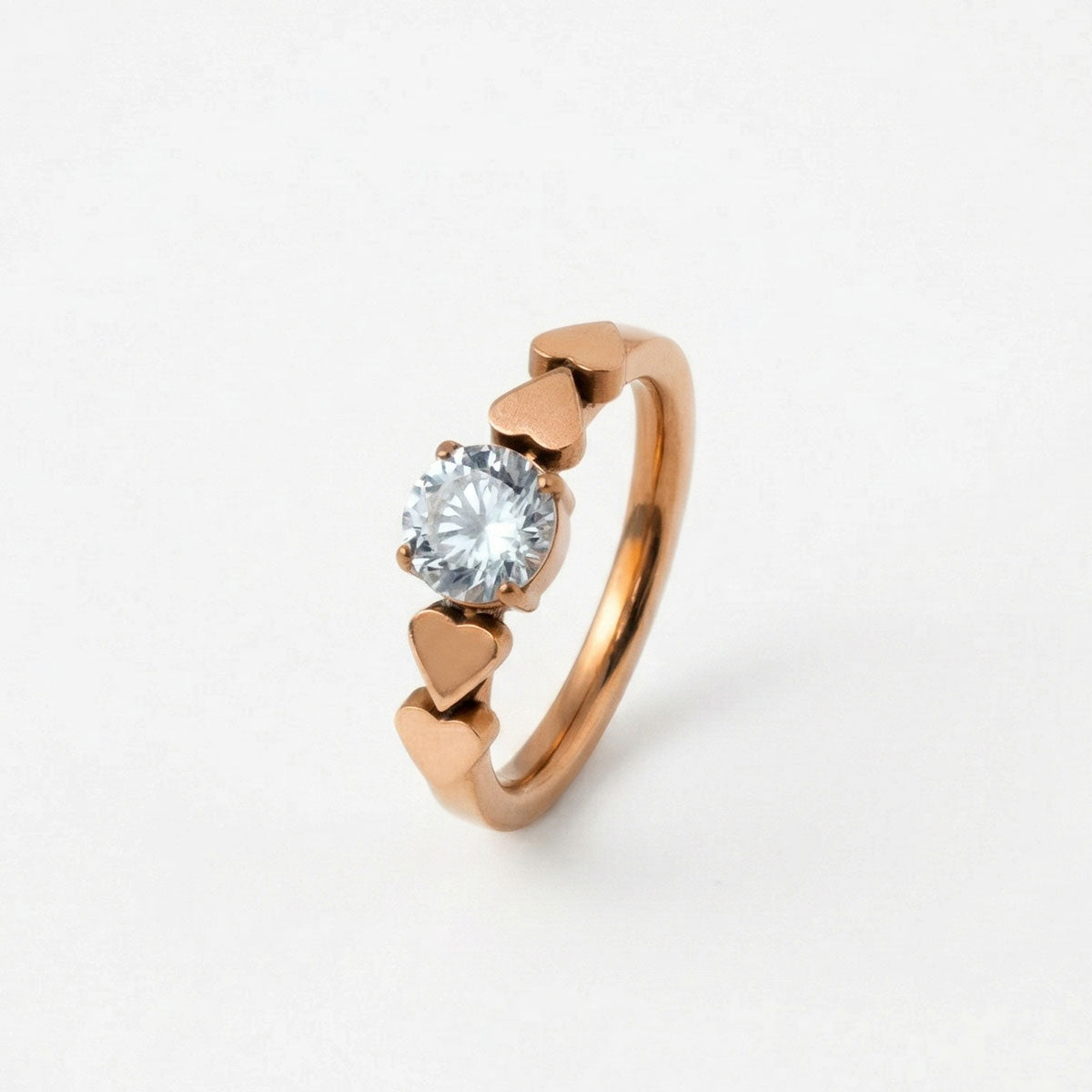 Anillo de compromiso en titanio enchapado en oro 18K de color oro rojo y dijes de corazones a los lados, sobre fondo blanco - producto de Joyería Monael