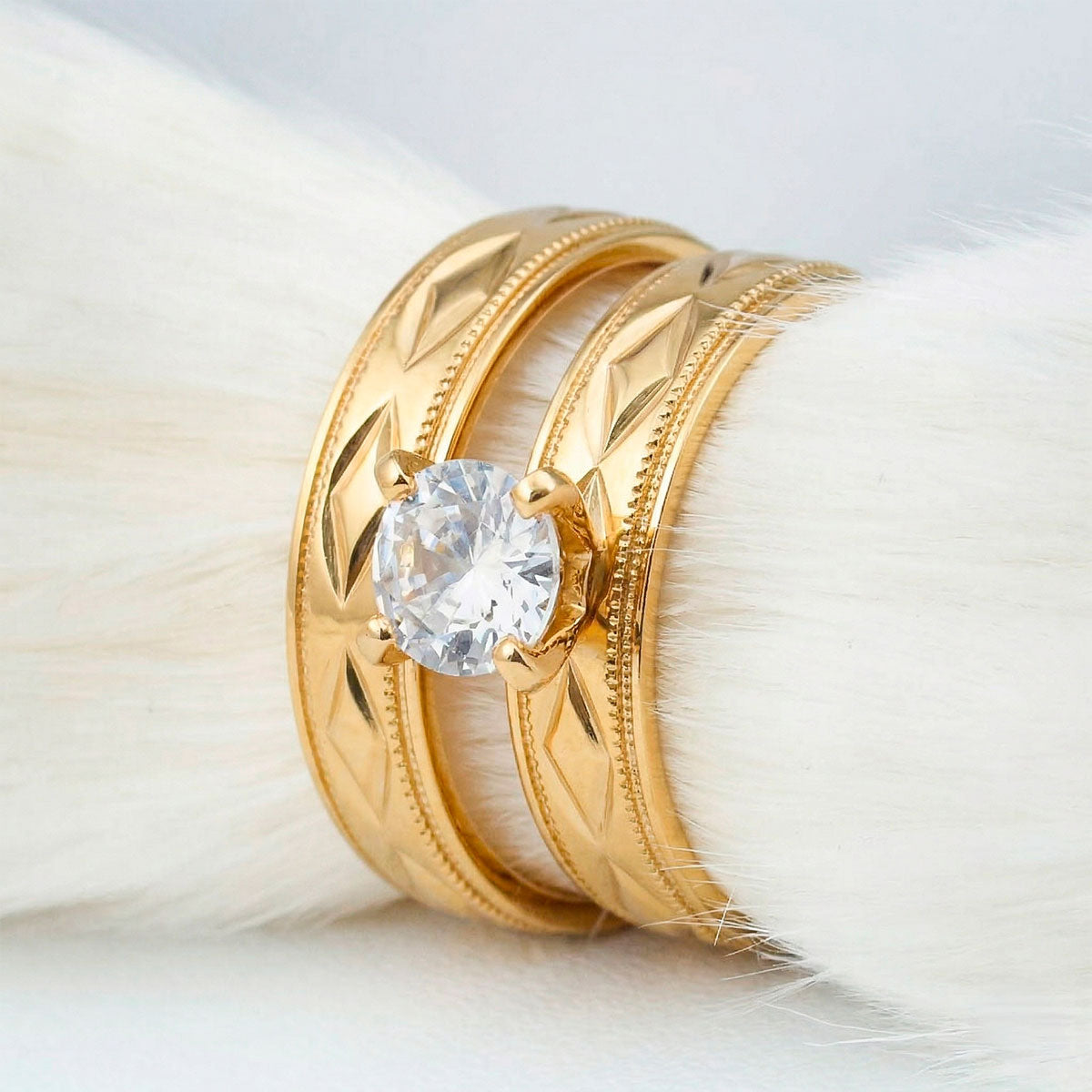Anillos para pareja en titanio con enchapado en oro amarillo, con un patrón de rombos grabados y bordes de microesferas. El anillo femenino incluye una piedra central brillante en engaste de cuatro puntas, código 4040.