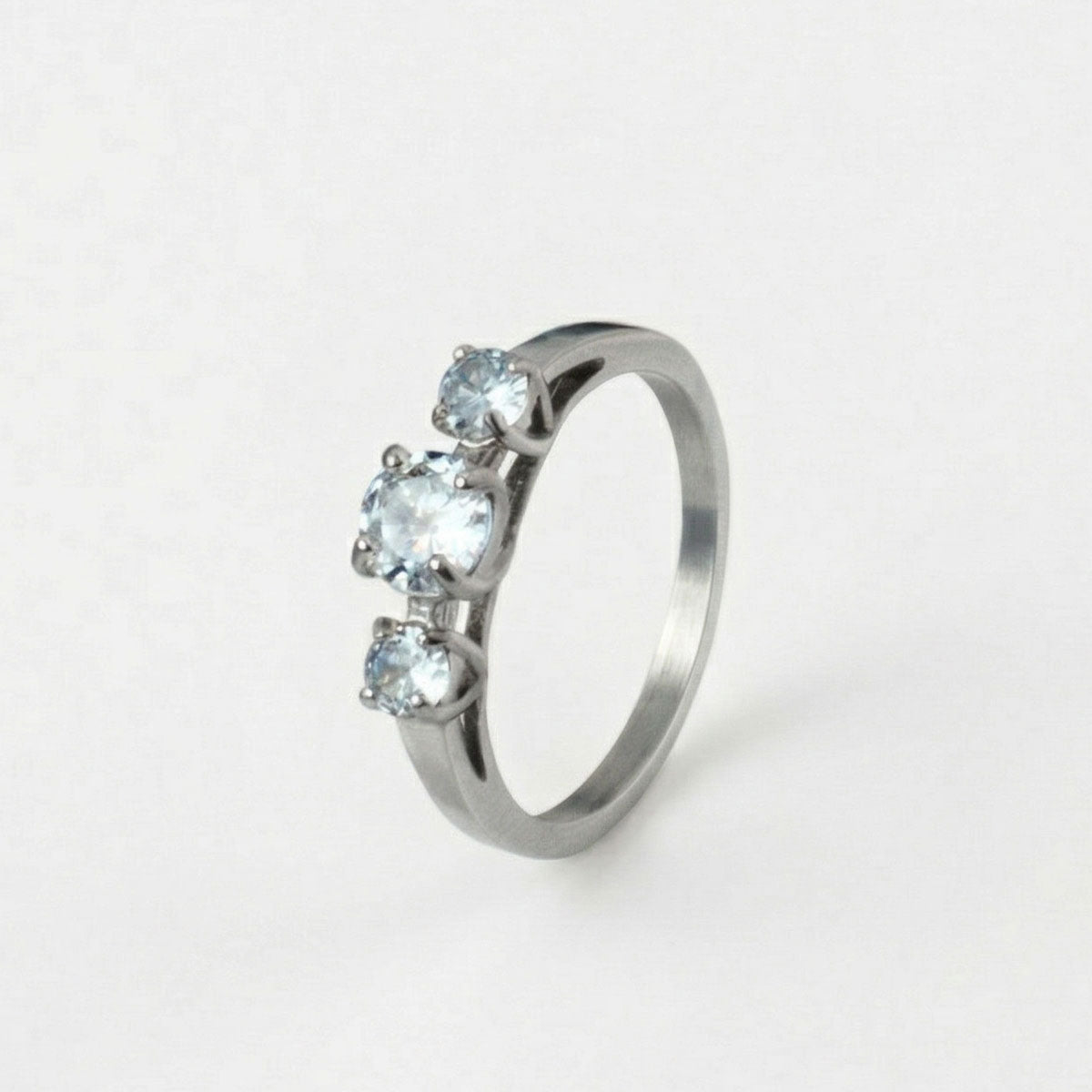 Anillo de compromiso en titanio enchapado en oro 18K de color plateado con tres piedras, sobre fondo blanco - producto de Joyería Monael