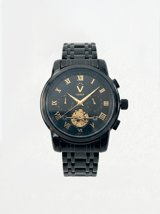 Reloj analógico para hombre en acero inoxidable color negro, esfera oscura con números romanos dorados, subesferas decorativas y ventana inferior con mecanismo dorado visible, caja de 42mm